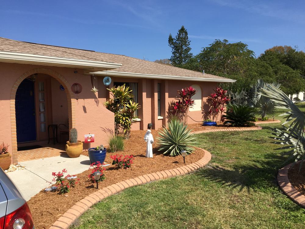Brick-edged planting bed and trimmed lawn in front of a coral stucco home