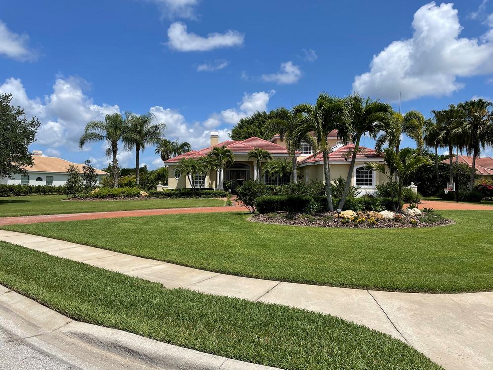 Stripe-mowed front lawn with crisp bed edging, royal palms and a tile-roofed home behind