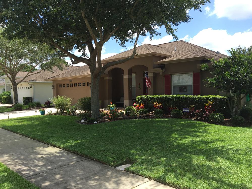 Front lawn and flower beds under a mature shade tree at a tan stucco home